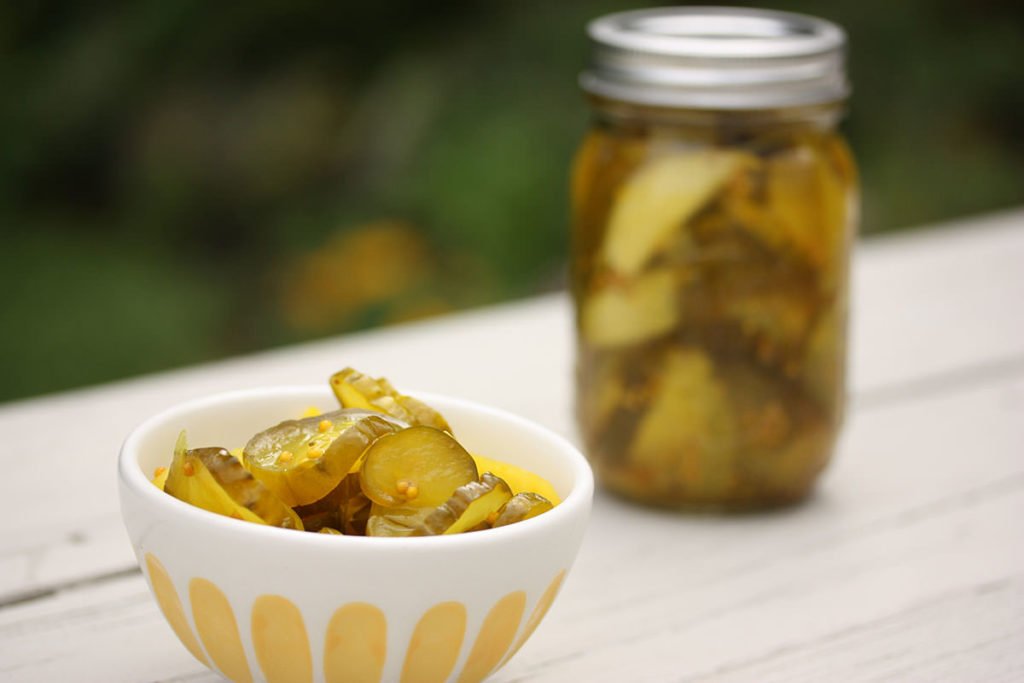 Image of a bowl of probiotic pickles in a bowl and pickles in a jar on a wooden table outdoors
