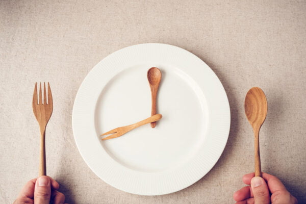 Image of an empty plate with a person holding wooden utensils to symbolize intermittent fasting